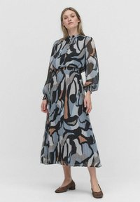 Langes, gefüttertes Kleid in einem abstrakten Muster aus Blau, Schwarz und Braun. Leichter Stoff, hoher Kragen, Knopfdetails und Ballonärmel.