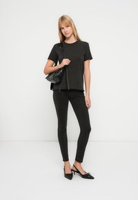 Svart t-skjorte med korte ermer kombinert med svarte smale jeans og svarte spisse flate sko. Antrekket inkluderer en strukturert svart håndveske.