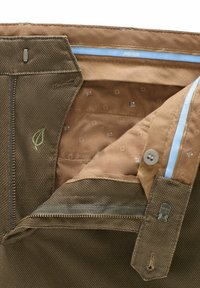 Gros plan sur un pantalon marron texturé dézippé avec une doublure beige à motifs, un bouton, une fermeture éclair et une étiquette de marque "Meyer" sur la ceinture intérieure.