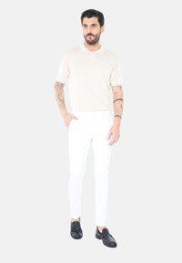 Polo shirt beige a costine con maniche corte, pantaloni bianchi slim-fit e mocassini neri. Focalizzati su linee pulite e design minimalista.