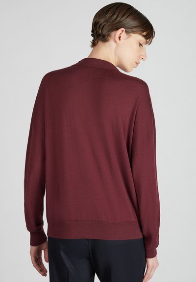 Burgundowy sweter z prążkowanym wykończeniem u dołu i przy rękawach, z długimi rękawami i luźnym krojem. Materiał wydaje się miękki i lekko lśniący.