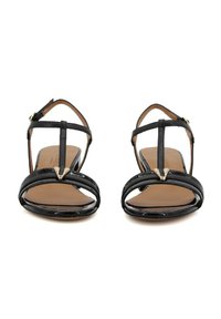 Sandali in pelle verniciata nera con design a T-strap, punta aperta e cinturini alla caviglia regolabili. Presentano un accento dorato nella parte anteriore.