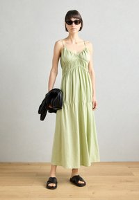 Pitkä, vaaleanvihreä mekko, jossa on säädettävät olkaimet, rypytetty yläosa ja hulmuava hame. Mustat suuret aurinkolasit ja clutch kädessä, litteät mustat sandaalit.