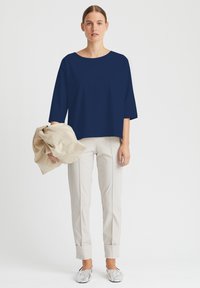 Navy-blaues Oversize-Oberteil mit weiten Ärmeln, kombiniert mit beigen, taillierten Hosen mit umgeschlagenen Säumen und metallischen Slippern.