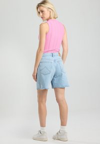 Vaaleanpunainen ribattu hihaton toppi on yhdistetty vaaleansinsisiin korkeavyötäröisiin farkkushortseihin, joissa on hapsut ja takataskut.