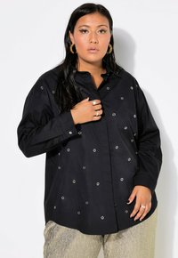 Camisa negra de botones hecha de algodón con acentos de ojales plateados dispersos por la tela, que presenta un corte relajado y un cuello.