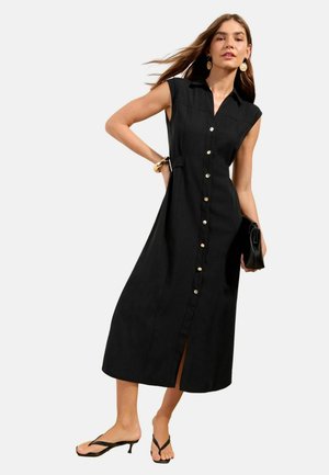 Nő ujjatlan fekete, elöl gombos midi ruhában, fülbevalóval, karkötővel, fekete borítéktáskával és fekete pántos, alacsony sarkú szandállal.