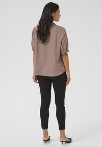 Maglietta ampia di colore marrone chiaro con maniche a sbuffo e polsini arricciati, abbinata a pantaloni neri aderenti e tacchi neri open-toe.