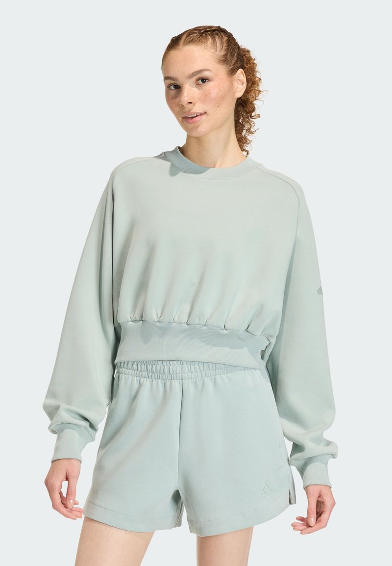 Light green sweatshirt with long sleeves and ribbed hem, paired with matching shorts. Material appears soft with a relaxed fit.