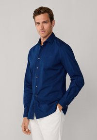 Camicia azzurra con bottoni in tessuto liscio, con colletto classico e bottoni coordinati, abbinata a pantaloni chiari.