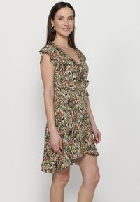 Bloemmotief jurk met een V-hals, korte gerimpelde mouwen, een getailleerde taille en een uitlopende rok. Kleuren zijn groen, oranje en zwart.