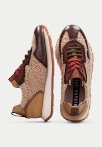 Sneakers z teksturowanym beżowym wełnianym korpusem, brązowymi skórzanymi akcentami, czerwonymi sznurówkami i beżową gumową podeszwą. Posiadają wyściełany kołnierz i unikalne przeszycia.