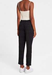 Pantalon noir à motifs avec taille élastique, présentant un design à pois blancs. Associé à un débardeur ajusté de couleur claire et des baskets blanches.