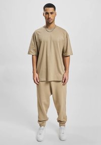 Beige katoenen T-shirt met korte mouwen, gecombineerd met beige joggers met elastische taille, met een ontspannen pasvorm, opgerolde enkels en witte sneakers.