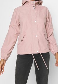 Ljusrosa huva med tryckknappar, elastiska ärmslut och två sidofickor. Justerbar dragkedja i fållen för en åtsittande look.