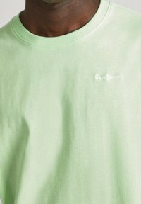 Světle zelené bavlněné tričko s kulatým výstřihem a jemnou texturou, s malým bílým vyšitým logem "Pepe Jeans" na prsou.