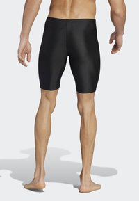 Shorts de bain noirs en matériau lisse, design ajusté, longueur mi-cuisse et détail de fermeture éclair à l'arrière. Texture douce avec des accents minimalistes.