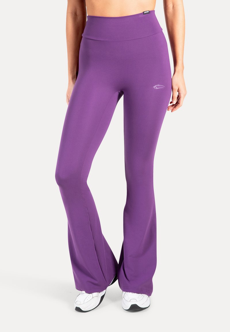 Leggings de sport évasés violets avec une taille haute et une texture lisse, dotés d'un petit logo à l'avant. Portés avec des baskets blanches.