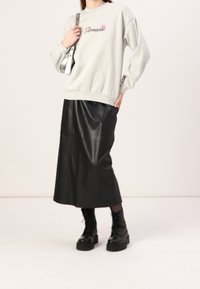 Maglione grigio con testo rosa "Romantic", abbinato a una gonna midi in pelle nera e stivaletti militari neri con lacci. Borsa argentata con tracolla.