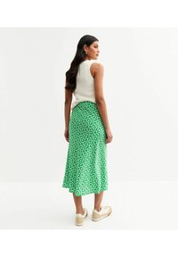 Jupe midi fleurie verte avec un design fluide, fabriquée en tissu léger, ornée de petites fleurs blanches et avec un ourlet qui tombe sous le genou.