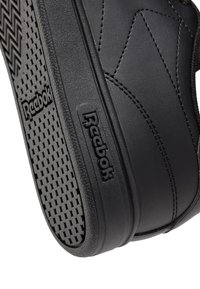 Zapatilla negra de Reebok con suela texturizada y parte superior de cuero liso, con detalles de costura y logotipo en el lateral.