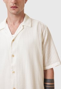 Kortsleeve skjorte i cremefarvet, med et tekstureret vævet mønster, klassisk krave og små frontknapper.