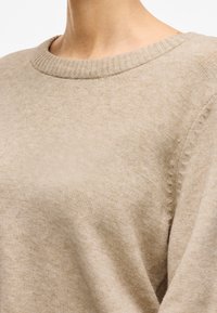 Suéter de punto color beige con un cuello redondo de canalé, textura suave y sutiles detalles en la costura del hombro.