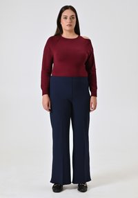 Maglione borgogna lavorato a maglia con design a spalla scoperta abbinato a pantaloni larghi blu navy. Tessuto morbido e vestibilità su misura. Mocassini neri completano il look.