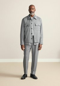 Gray wool blazer with two chest pockets and buttons, paired with matching trousers. Black shoes complete the outfit. Textured, tailored fit.