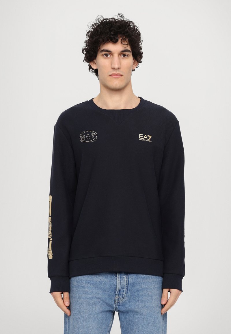 Jūrnieka kreklu izgatavots no teksturēta auduma, ar zeltītu EA7 logo uz krūšu un piedurknēm. Apaļa apkakle un ribota piedurkne.