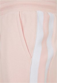 Rozā treniņbikses ar mīkstu tekstūru, ar sānu kabatu un baltām svītrām. Jostasvieta ir ribota, lai nodrošinātu ciešu fit.