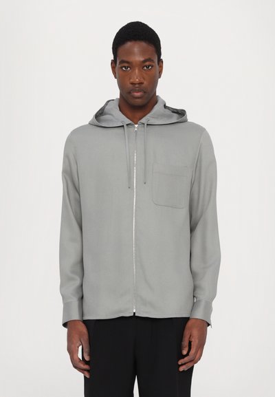Lys grå zip-up hoodie i blødt stof med en frontlomme og justerbar snorhætte, der har en glat overflade og en afslappet pasform.
