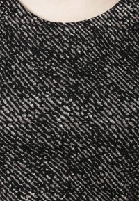 Tissu noir et crème à motif avec un design texturé et ondulé, comportant un col rond et une surface lisse.