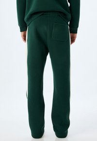 Grüne Jogginghose mit seitlichen cremefarbenen Streifen, elastischem Bund und einer Gesäßtasche. Weicher Stoff, lässige Passform, tapered Beine.