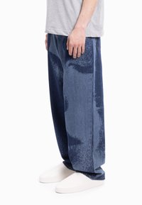 Wyblakłe niebieskie dżinsy o luźnym kroju i unikalnej wzorzystej fakturze, zestawione z gładkimi białymi butami wsuwanymi.