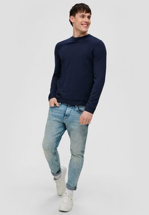 Navy long-sleeve knit top paired with light blue distressed jeans and white sneakers; rounded neckline and fitted silhouette.