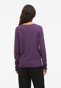 Maglione viola a maglia con maniche lunghe, scollatura rotonda e orlo a costine. La texture appare morbida e leggermente oversize.