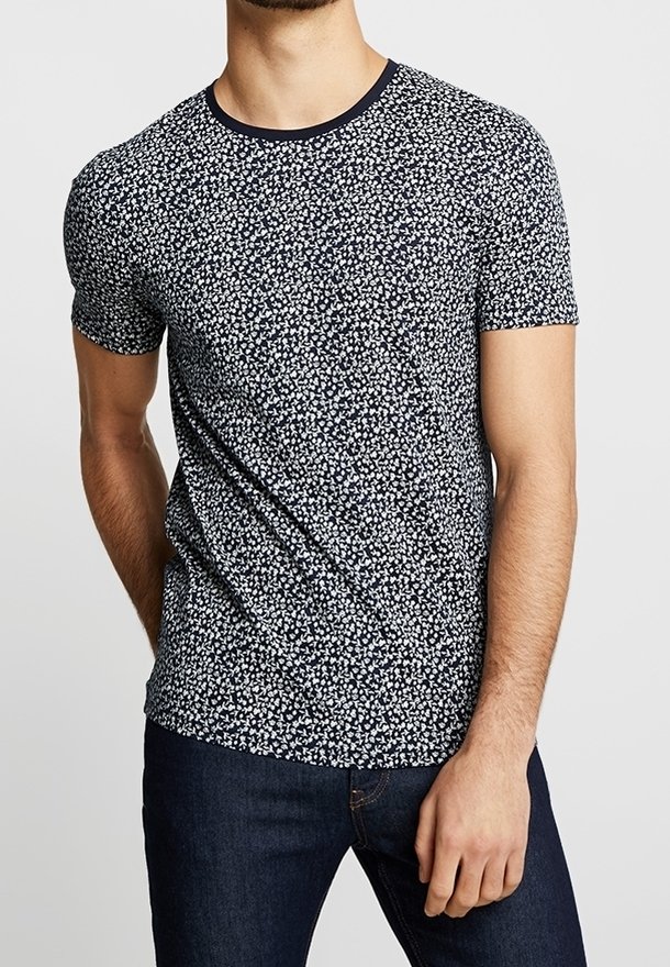 Krátký rukáv tričko v námořnické látce s květinovým vzorem v bílé barvě. Má kulatý výstřih s kontrastním lemem.