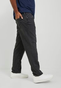 Jeans en denim gris foncé avec un design à coupe droite, un léger délavage et des poches arrière. Portés avec des baskets blanches.