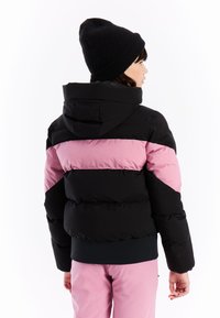 Pufferjack met een capuchon in zwart en roze, met een gewatteerd ontwerp en elastische manchetten, gedragen met een zwarte gebreide beanie.