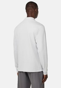 Camisa polo blanca de manga larga con una textura en la tela, que presenta un cuello y puños acanalados, vista desde la parte posterior.