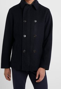 Abrigo de mezcla de lana en color navy con un frente de doble botonadura, cuatro botones, cuello puntiagudo y bolsillos laterales. Ofrecido en un ajuste estructurado y entallado.