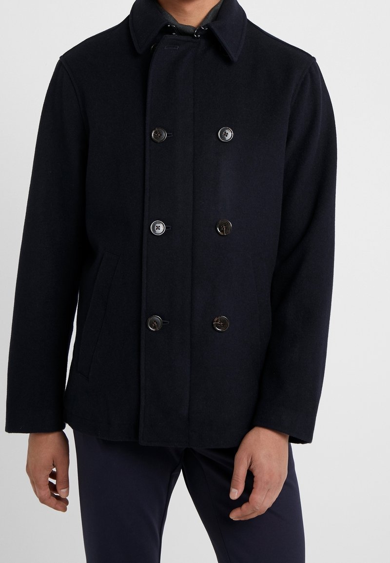 Abrigo de mezcla de lana en color navy con un frente de doble botonadura, cuatro botones, cuello puntiagudo y bolsillos laterales. Ofrecido en un ajuste estructurado y entallado.