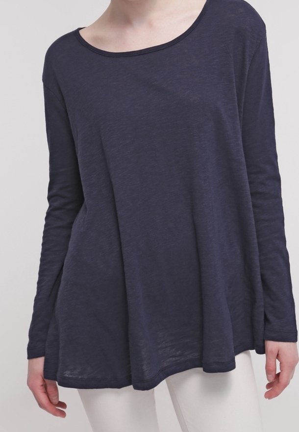 Granatowa bluzka z długimi rękawami o szerokim dekolcie, o luźnym kroju i lekkim, teksturowanym materiale. Posiada zaokrąglony dół i boczne rozcięcia.