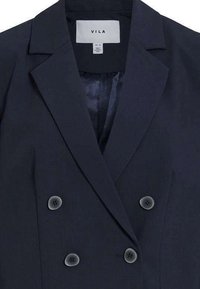 Blazer croisé bleu marine avec revers crantés, tissu texturé et boutons ronds noirs. Intérieur doublé visible. Étiquette de marque : VILA.