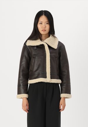 Chaqueta corta de cuero marrón con un cuello y puños de shearling crema, que cuenta con dos bolsillos frontales y un acabado suave.
