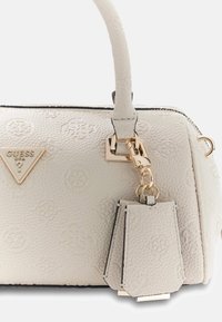 Borsa bianca con texture, rifinita con dettagli in oro, caratterizzata da una placca con logo e un accessorio staccabile. Chiusura con cerniera lungo la parte superiore.