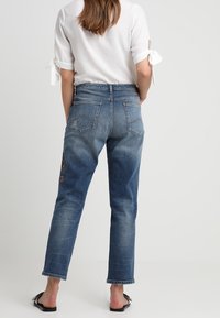 Siniset farkut suorilla lahkeilla, joissa on kaksi takataskua, kevyttä kulutusta ja vasemman reiden brodeerausdetaili.