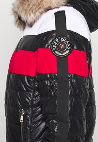 Vadderad jacka med en färgskala av svart, röd och vit, glansig textur, pälskantad huva och "River Island"-logotyp på ärmen.