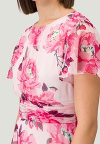 Gros plan sur une robe sans manches avec des motifs floraux roses et rouges, dotée d'une taille froncée et d'un tissu léger et fluide.